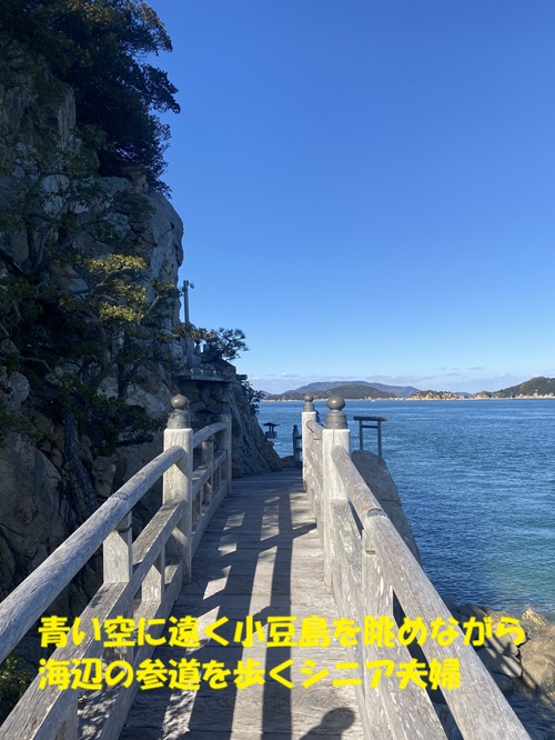 青い空に遠く小豆島を眺めながら海辺の参道を歩くシニア夫婦